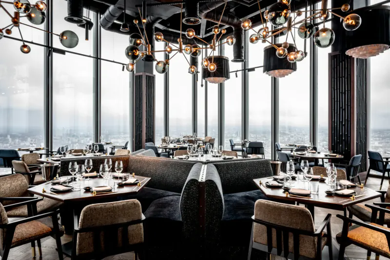 Lucky Cat by Gordon Ramsay: Elegant high-rise dining room with panoramic city views, curved black booths, globe pendant lights, and set tables.