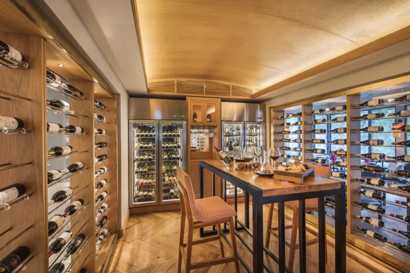 Elegant wooden wine cellar with racks of bottles, glass doors, and a high black bar table with stools at Anantara Iko Mauritius Resort.