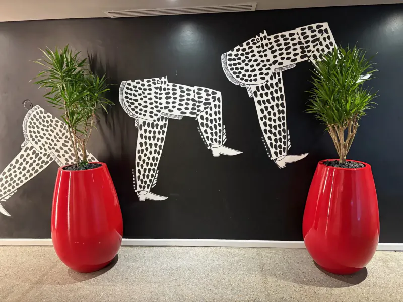 Black wall art of white polka-dot trousered legs beside red pots with green plants in hotel lobby