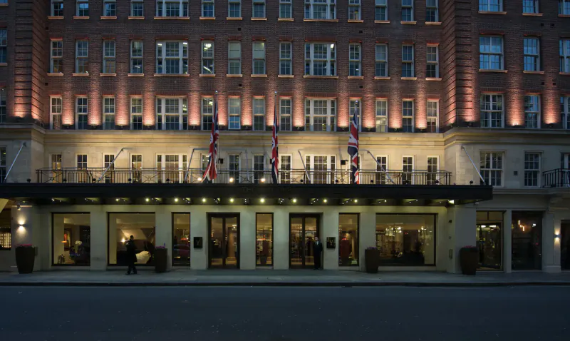 The May Fair Hotel, a grand London icon, facade lit at night with Union Jack flags and balcony.