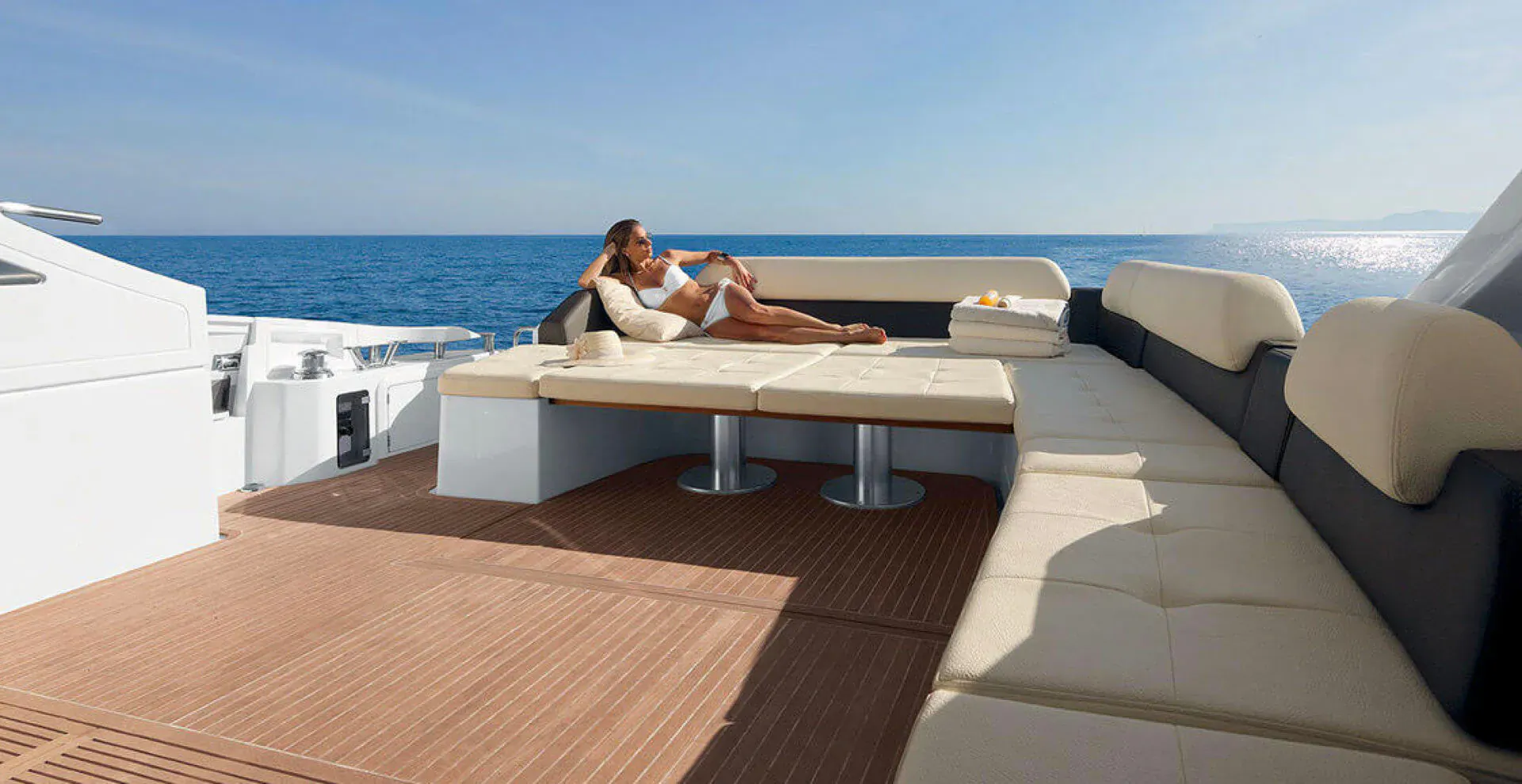 Woman lounging on cream and black leather bench on white yacht deck overlooking blue ocean