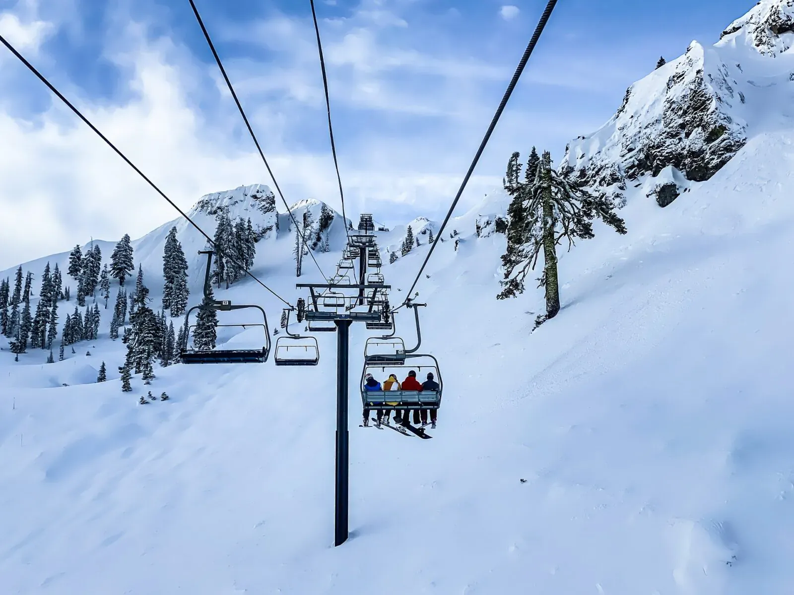 Ski lift carrying passengers up snowy mountain slope with pine trees under blue sky