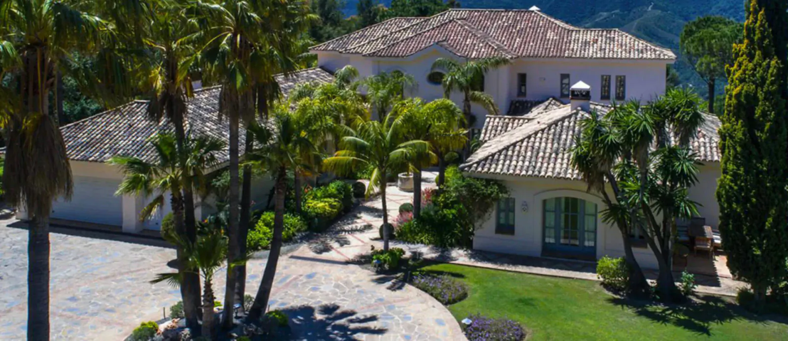 Aerial view of premium luxury villa at Marbella Mountain Resorts, with terracotta roofs, palms, pool, and lush gardens.