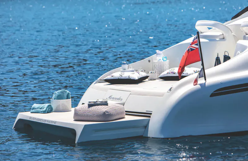 White luxury yacht stern on blue sea with UK flag, teal towels, white cushions on swim platform