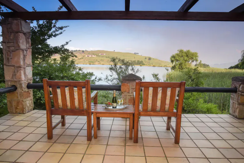 Two wooden chairs and small table with wine bottle on tiled patio deck overlooking lake and hills at Walkersons Hotel & Spa