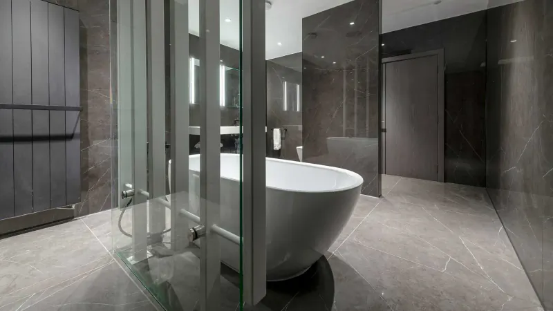 Modern luxury bathroom with freestanding white bathtub in glass shower enclosure, gray marble walls and tiled floor