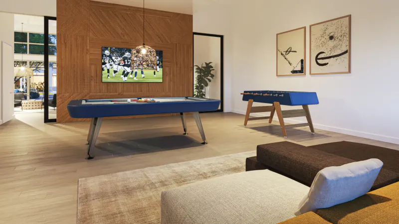 Modern lounge at Ariva Serviced Residences with blue foosball table, soccer on wall TV, wood wall, art, plants, sofa.