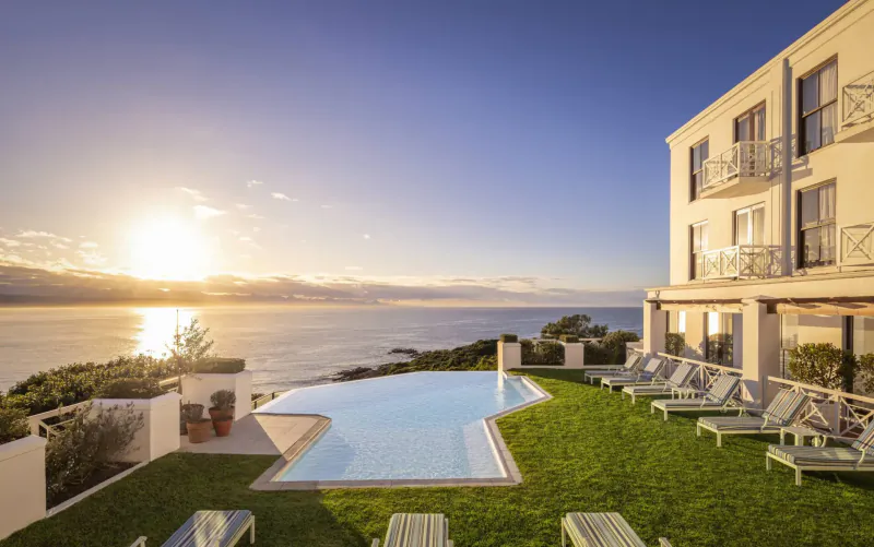 Infinity pool and lounge chairs at The Plettenberg Boutique Hotel overlooking ocean at sunset