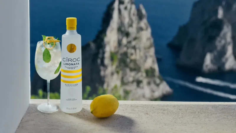 Cîroc Limon vodka bottle and lemon garnish cocktail glass on ledge overlooking Amalfi Coast sea cliffs