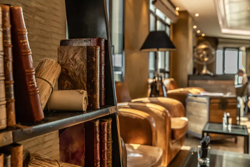 Cozy lounge in Saint-Malo's Nouveau Monde hotel with leather armchairs, vintage bookshelves, golden Buddha statue, and warm lighting.