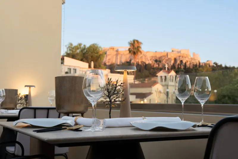Elegant table set with wine glasses at Makris Restaurant, overlooking Acropolis at sunset, Athens.