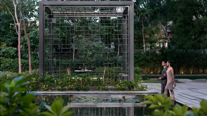 Couple in formal attire walks by modern lattice pavilion with trees, lily pad pond, and lush greenery at Four Seasons Bengaluru.