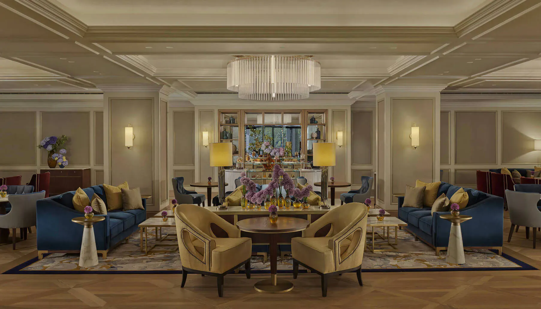 Elegant Carlton Tower Jumeirah Hotel lobby with blue velvet sofas, gold chairs, large floral arrangements, and chandeliers.