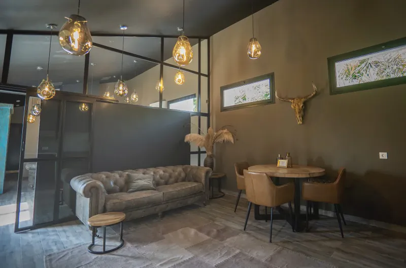 Cozy lounge at La Vuelta Boutique Hotel with tufted gray sofa, round table, chairs, pendant lights, potted palms, and longhorn skull.