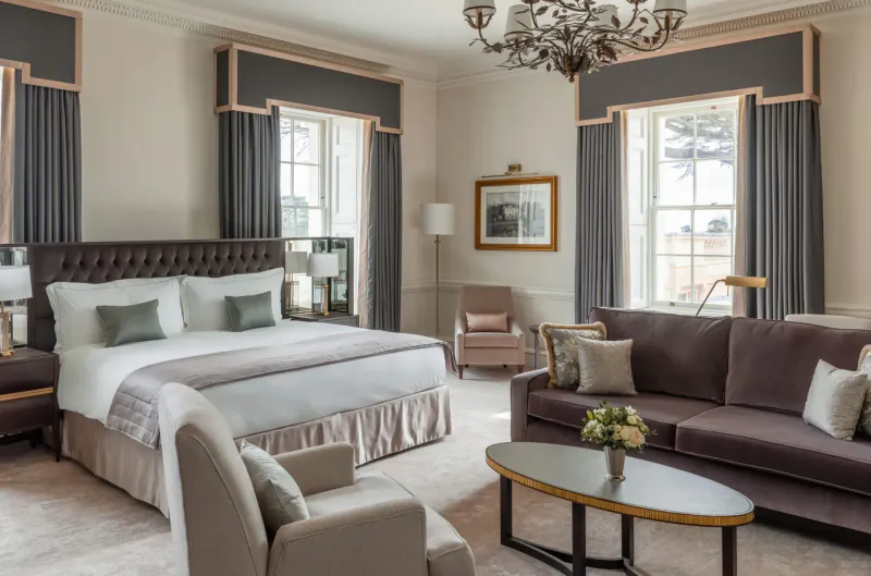 Elegant luxury hotel suite at The Langley with king bed, velvet sofa, chandelier, and flowers.