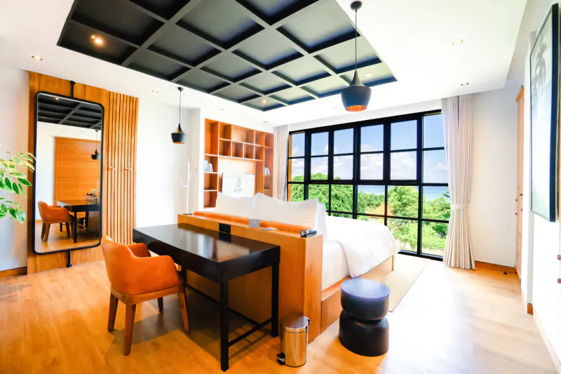 Luxurious modern bedroom in Secana Beachtown Bali with ocean view, wooden desk, orange chair, and pendant lights.