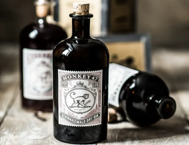 Three corked amber glass bottles of Monkey 47 gin with monkey labels on wooden surface.