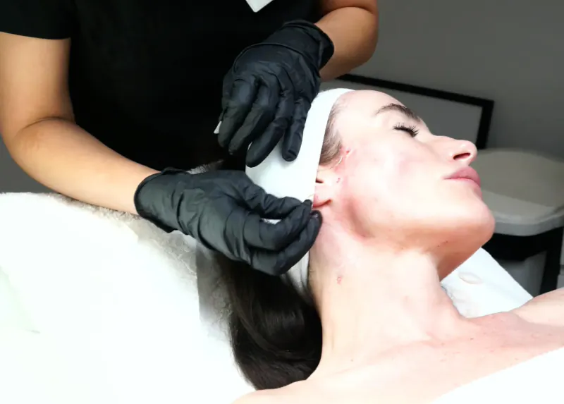 Dr Kubicka in black gloves wraps white bandage around client's neck on treatment bed for natural lift