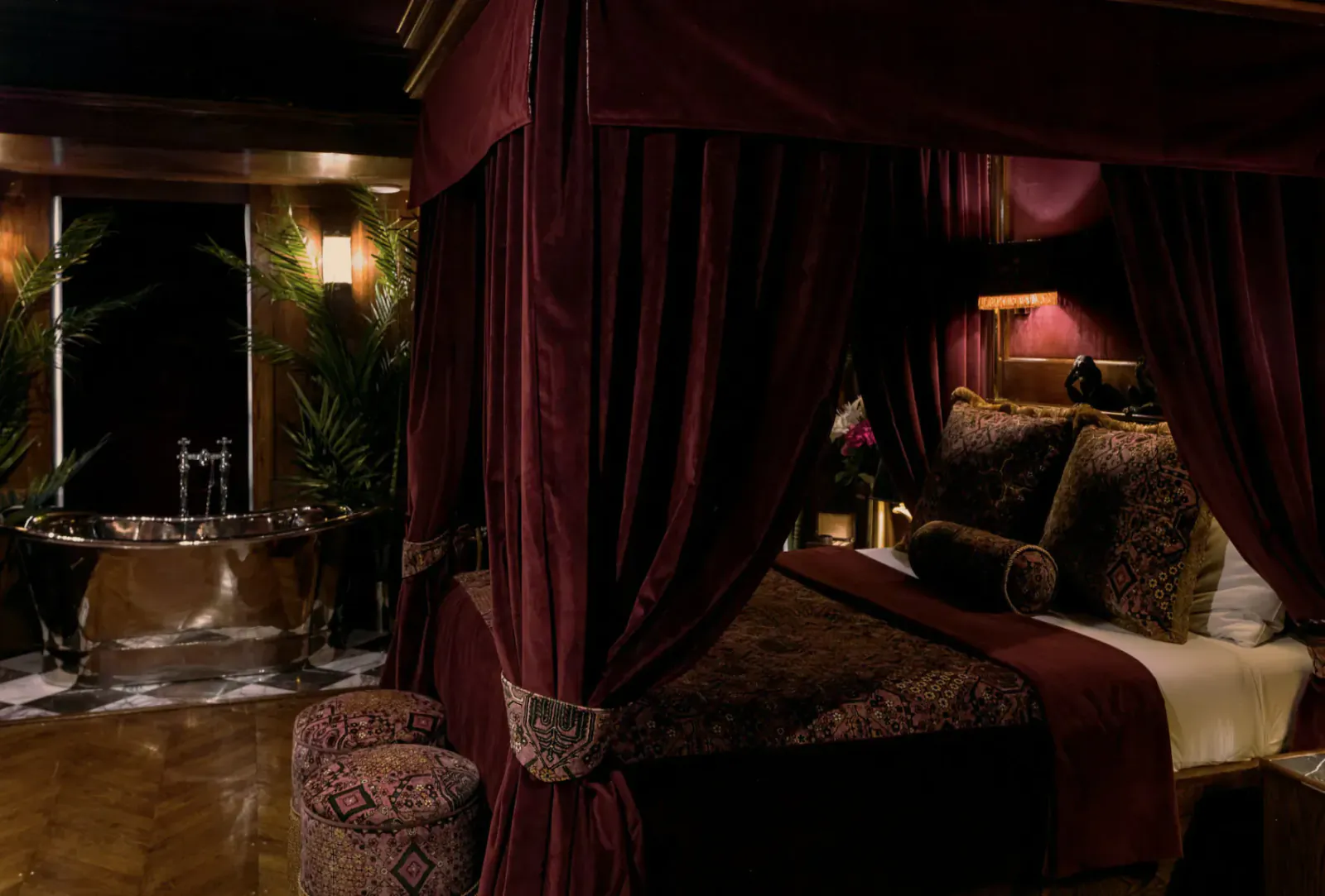 Luxurious burgundy four-poster bed and clawfoot bathtub in opulent Edinburgh hotel suite at House of Gods.