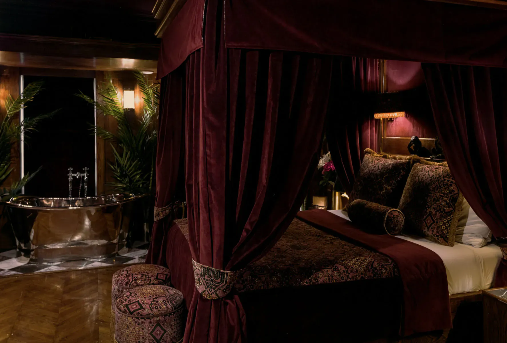 Luxurious burgundy four-poster bed and clawfoot bathtub in opulent Edinburgh hotel suite at House of Gods.
