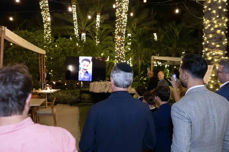 Crowd at outdoor evening event under string lights and palms watches man on screen; Continuum childhood cancer society gallery
