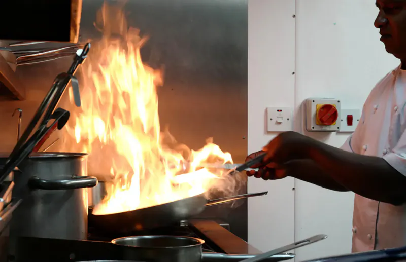 Chef in white uniform stir-frying food with high flames in a wok at Indian restaurant kitchen