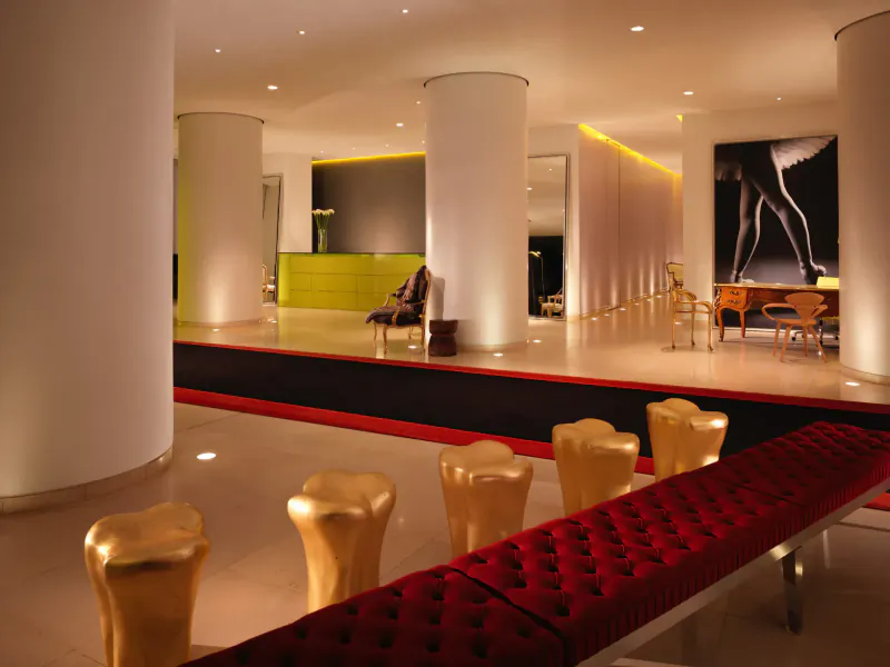 Modern hotel lobby at St. Martins Lane with white columns, gold stools, red bench, green reception, and large black-and-white leg artwork.