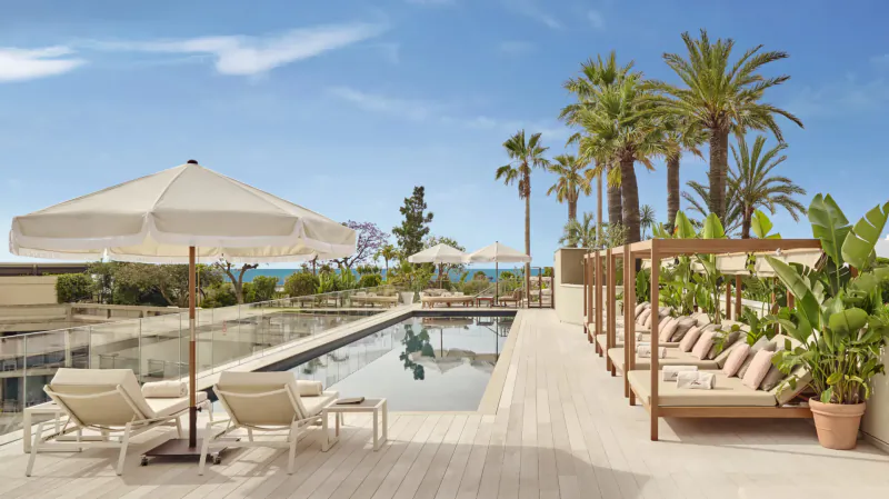 Fairmont Monte Carlo rooftop infinity pool with loungers, white umbrellas, palms, and sea view under blue sky.