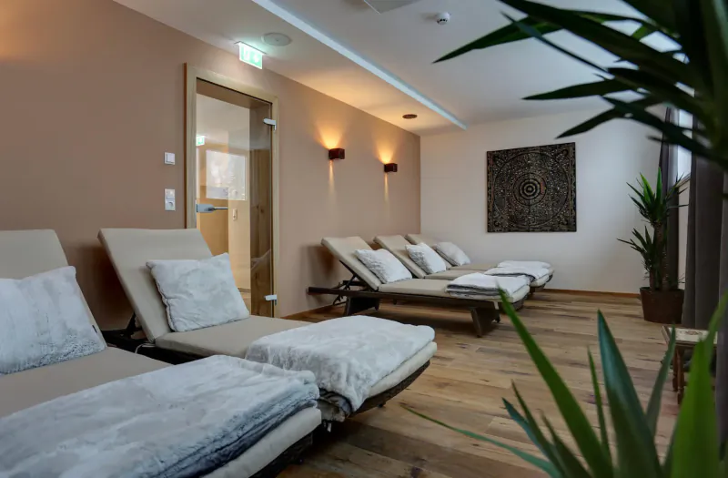 Luxurious spa lounge at Hotel Kösslerhof with beige reclining chairs, plants, wood floor, and sauna door.
