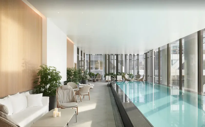 Modern indoor infinity pool at Pan Pacific London with lounge chairs, plants, and city views