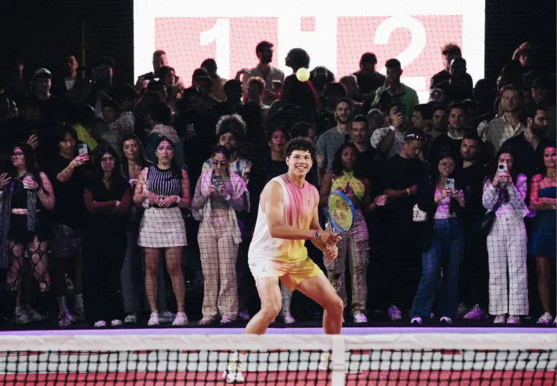 Athlete in pink tank top and shorts hits pickleball with paddle on court amid cheering crowd, scoreboard shows 1:2