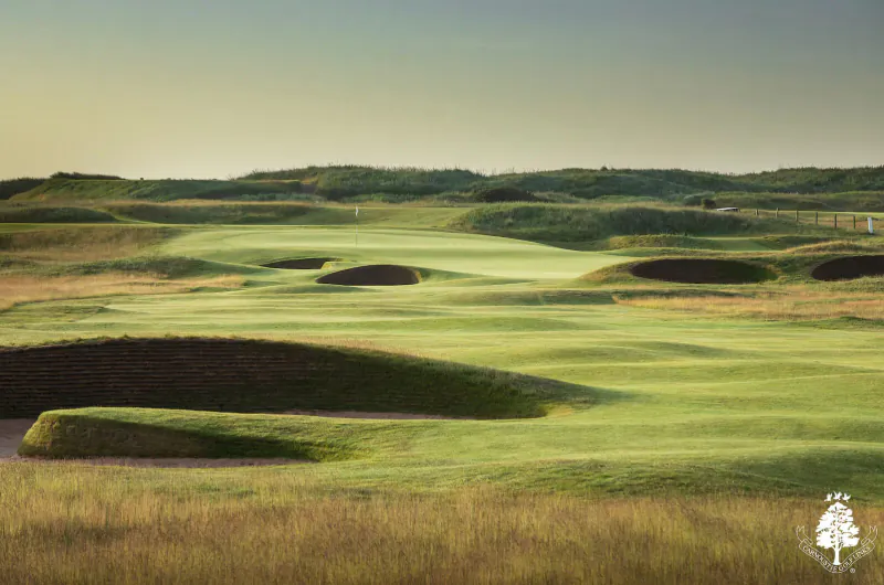 Carnoustie Links golf course at sunset with rolling green fairways, deep bunkers, and grassy dunes.