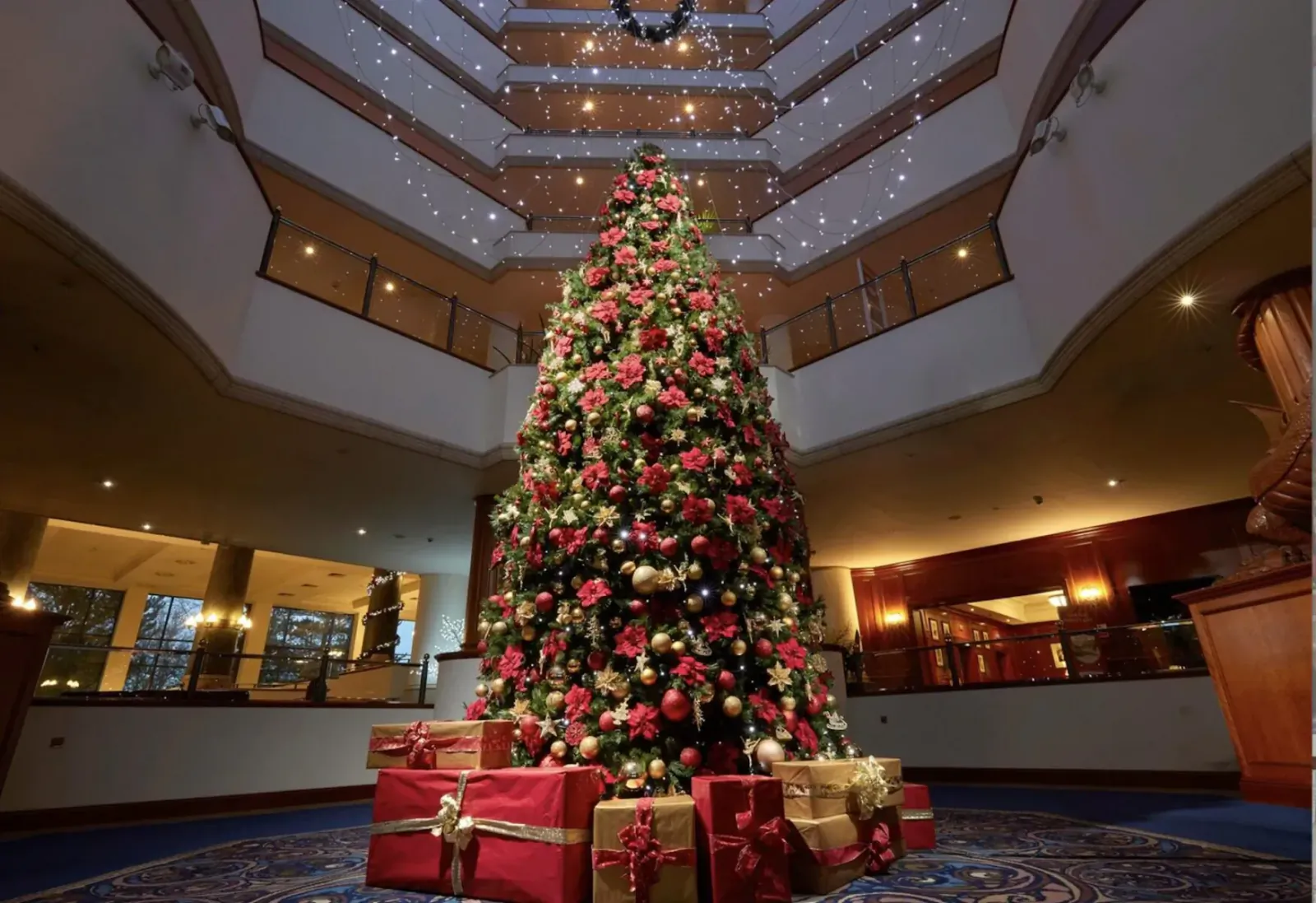 Towering decorated Christmas tree with red ornaments and wrapped gifts in grand atrium of Celtic Manor Resort lobby