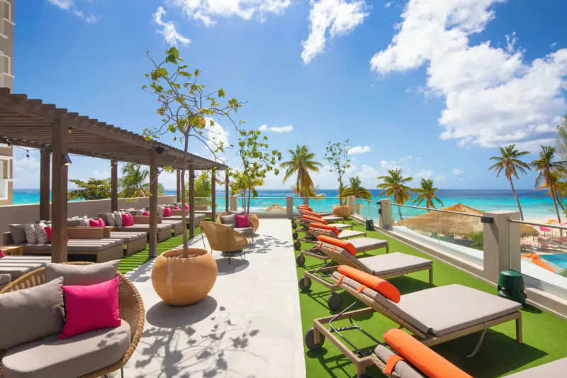 O2 Beach Club & Spa rooftop lounge with orange loungers, pink cushions, palms, and turquoise sea view in Barbados
