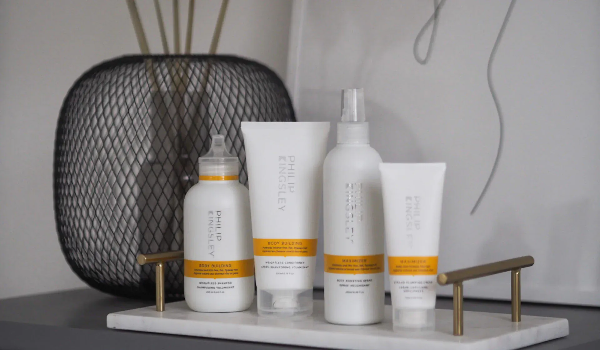 Philip Kingsley white hair care products on marble tray with black wire basket and bamboo, featuring 'Bigger, bouncier, beautiful hair'.