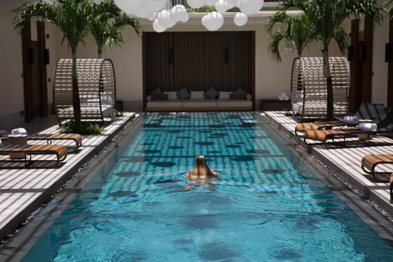 Woman swimming in turquoise pool at Silversands Grenada, surrounded by palms, loungers, and hanging lanterns