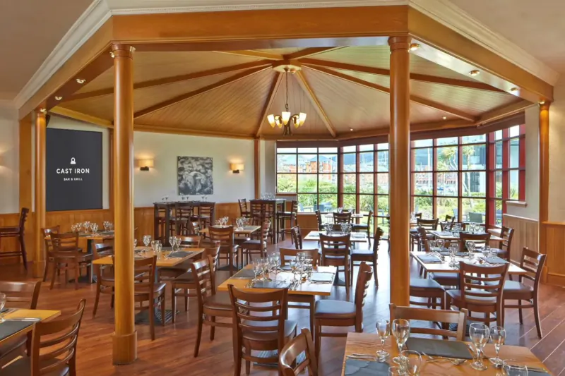 Spacious wooden dining room at Delta Hotel by Marriott Swansea with tables set for meals and garden view.
