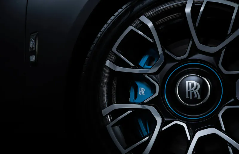 Close-up of Rolls-Royce Black Badge Ghost wheel with blue RR badge and calipers on black car