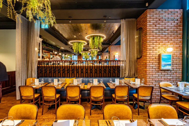 Amalfi Ristorante dining area with orange chairs, wooden tables, hanging plants, brick walls, and balcony.