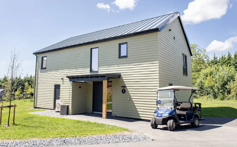 Beige modern cabin with black roof at Bluestone National Park Resort, golf cart parked outside amid green countryside.
