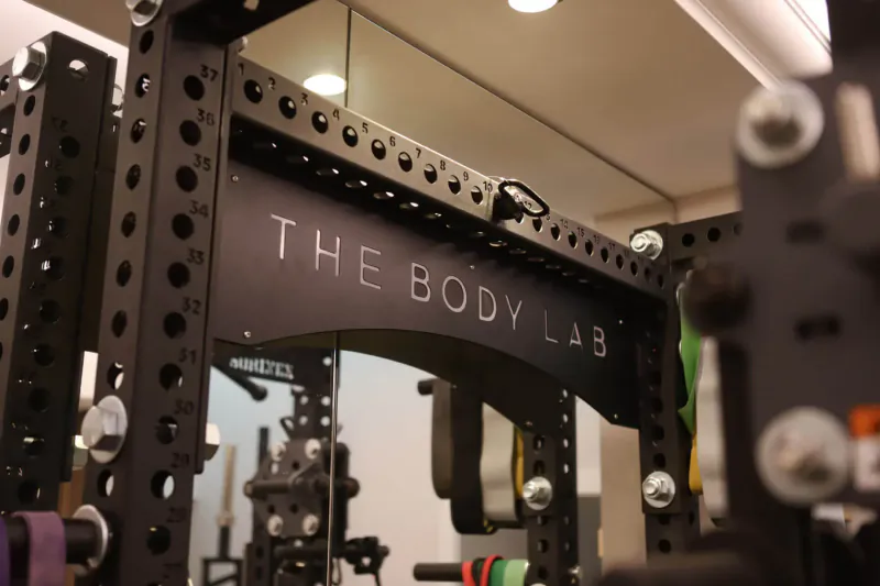 The Body Lab gym with black squat racks, mirrors, green bands, and weights in modern setting