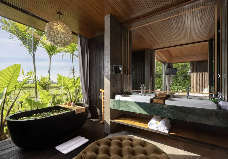 Luxurious Bali bathroom with black bathtub, green marble vanity, towels, and tropical garden view through large windows.