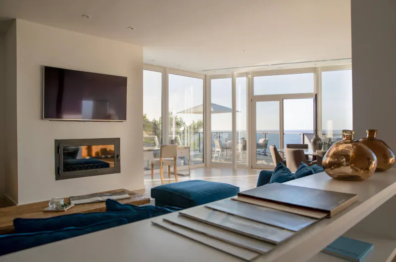 Modern luxury hotel living room with fireplace, TV, blue sofa, magazines on shelf, sea view balcony in Mallorca.