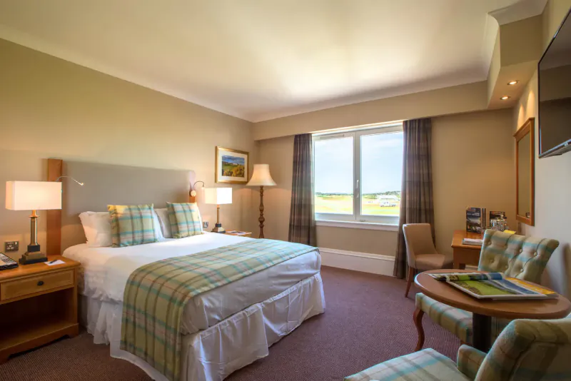 Luxurious hotel room with plaid bed, lamps, chairs, golf course view from window in Carnoustie, Scotland