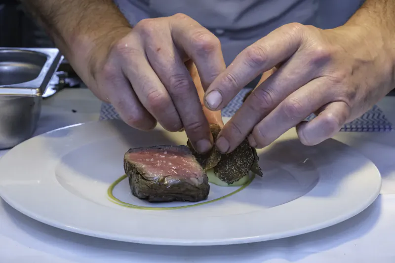 Chef's hands placing seared steak with green sauce swirl and herb on white plate at Nut Tree Inn