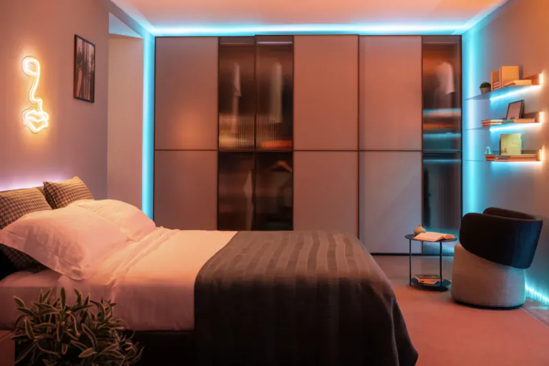 Modern bedroom with neon music note wall light, blue LED-lit wardrobe, bed, and shelf lights.