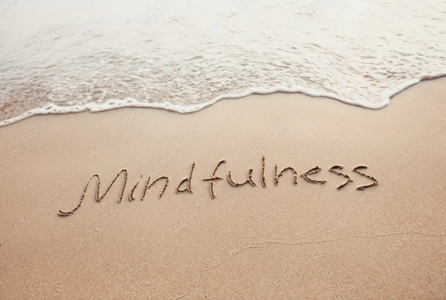 Word 'Mindfulness' written in sand at the beach with waves in the background.