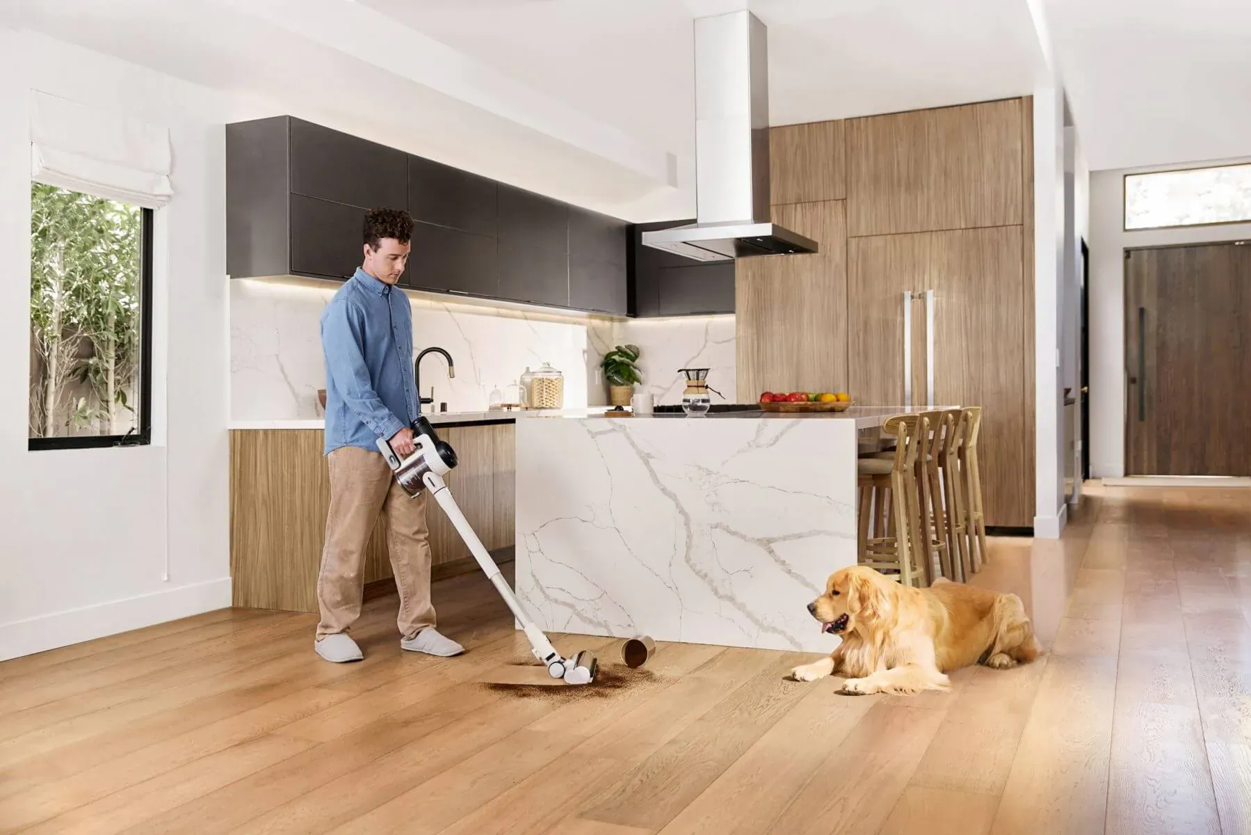 Man using Tineco PURE ONE S15 cordless stick vacuum on kitchen floor beside golden retriever dog