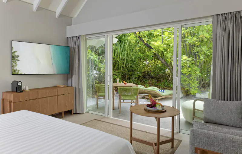 Spacious Amari Raaya Maldives villa bedroom with open doors to lush tropical garden, beach view, and pool.
