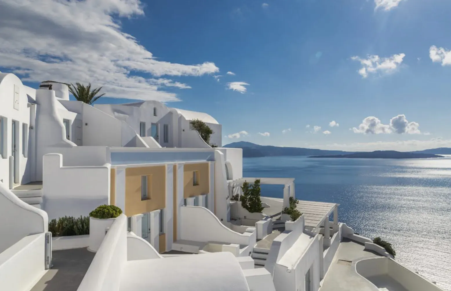 White luxury homes with plants perched on cliff overlooking blue Aegean Sea, Santorini Greece